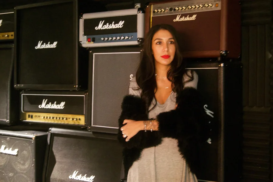 Lily Rivers in fur in front of Marshall amplifier stacks