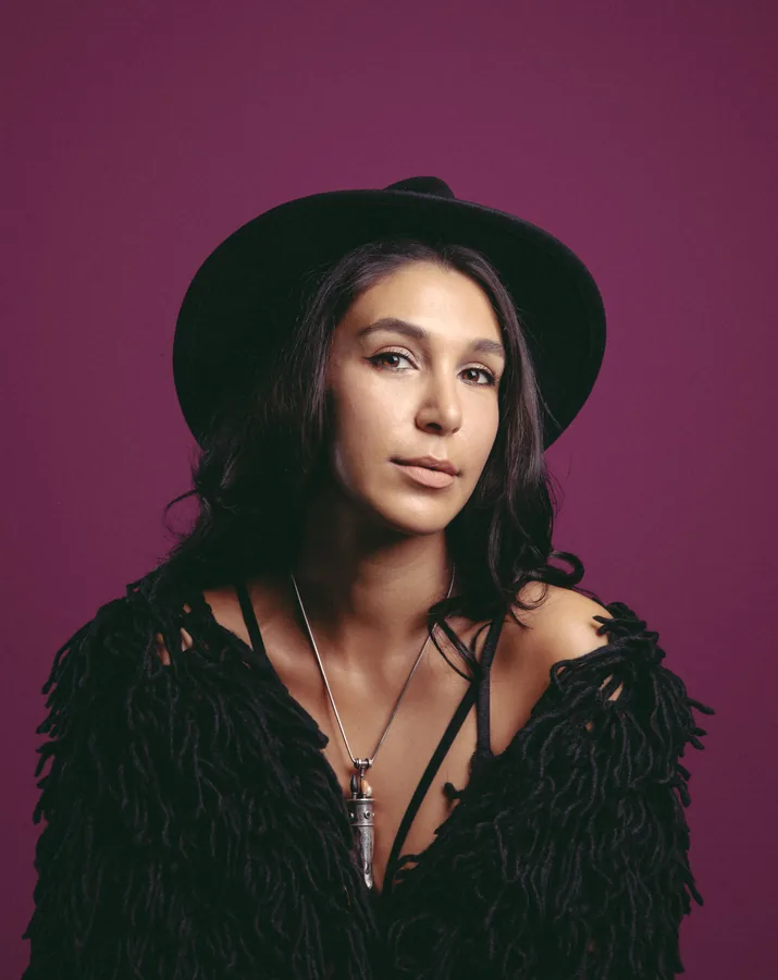 Lily Rivers in a black hat against a plum wall